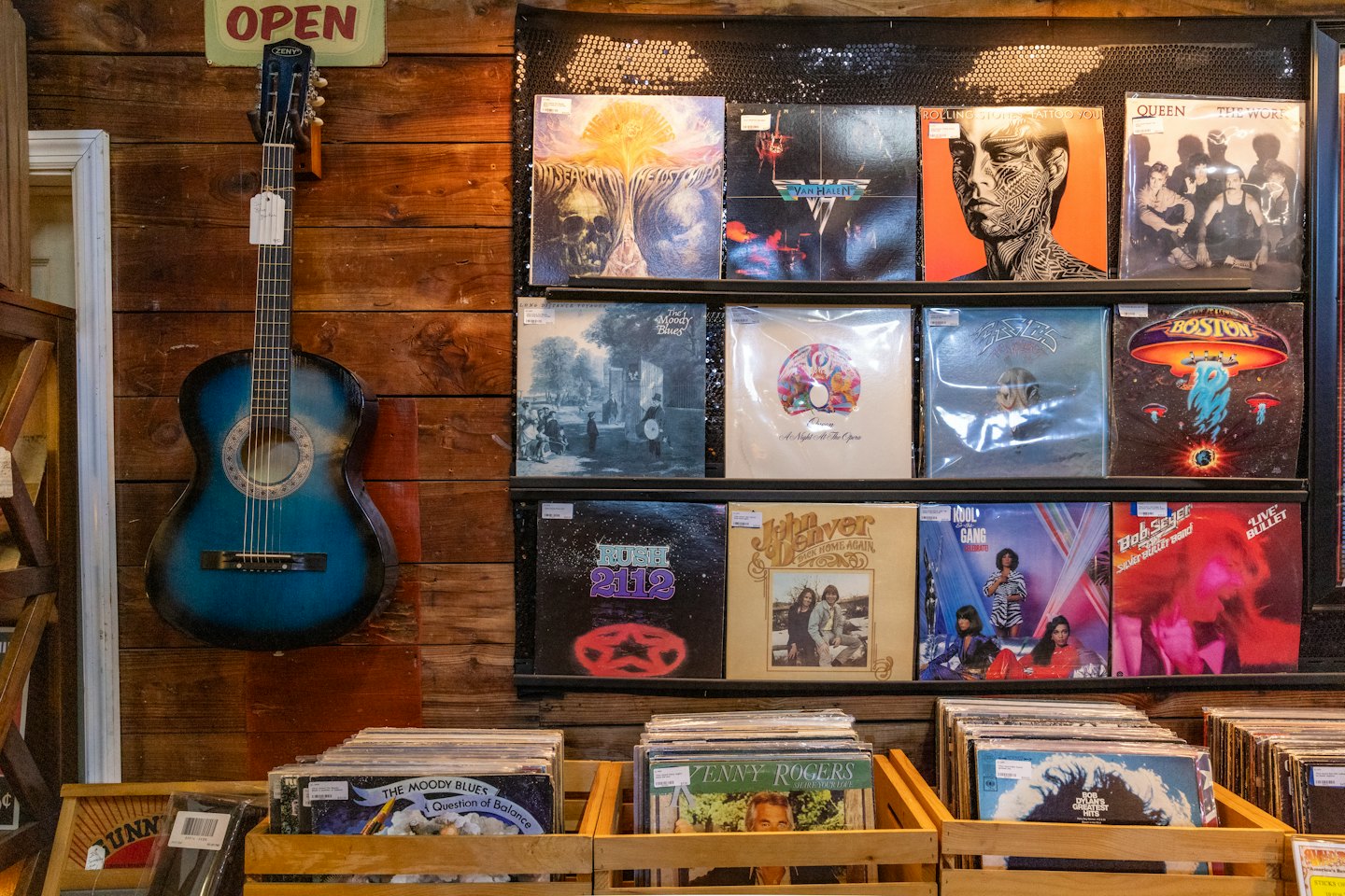 Blue acoustic guitar on a wooden plank wall with record albums.