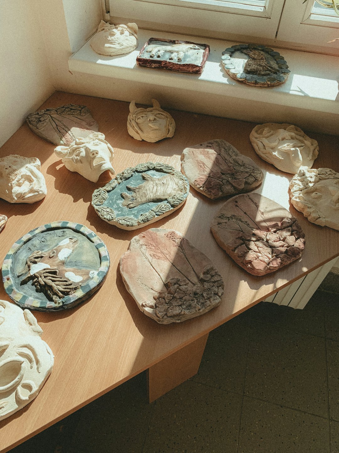 Handmade clay sculptures and reliefs arranged on a wooden table.