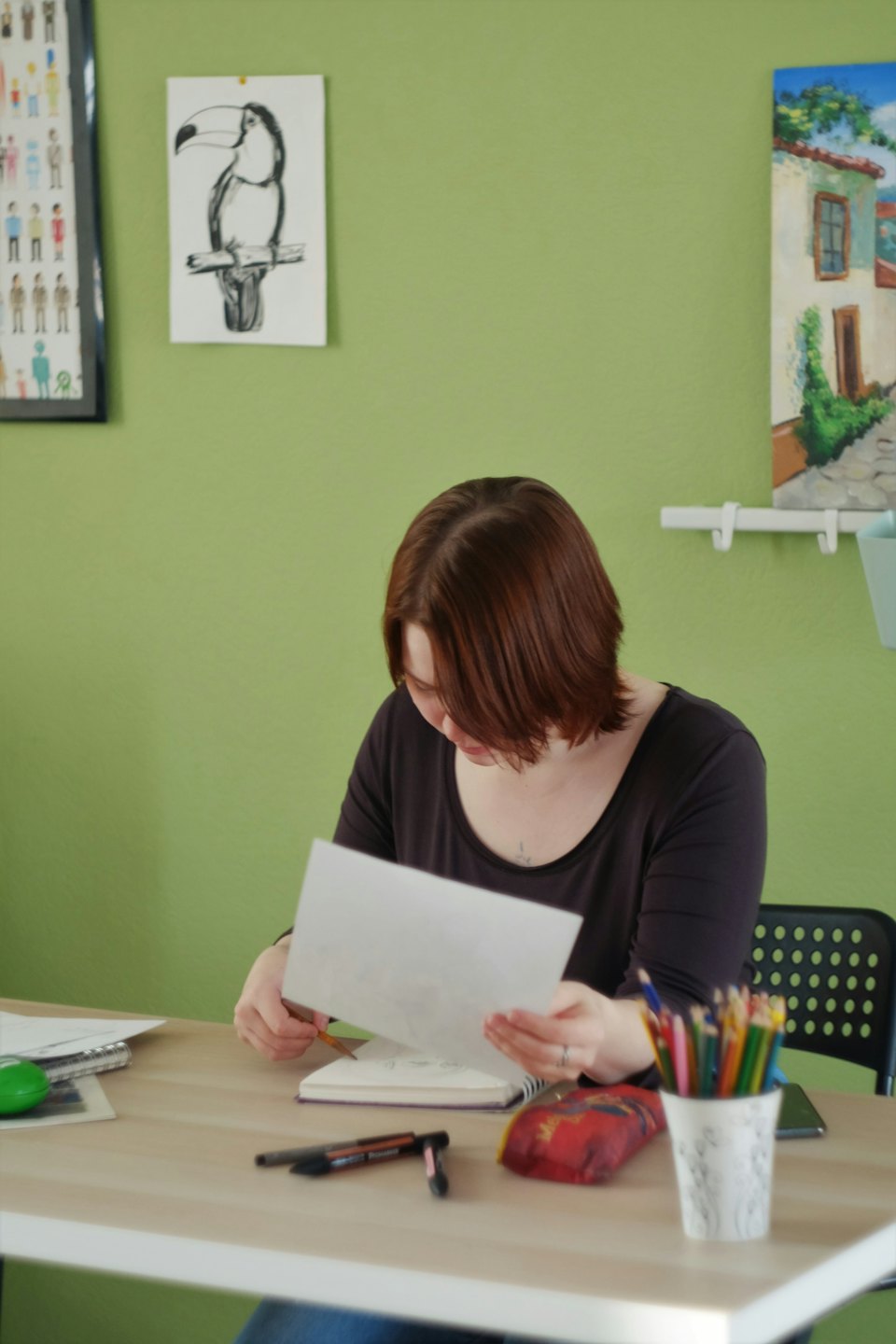 Person sketching at a desk surrounded by art supplies.