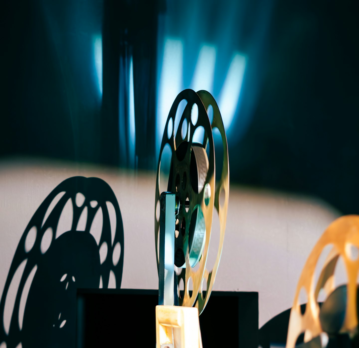 A vintage metal film reel stands against a grey wall.